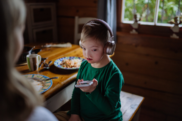 A boy with Down syndrome with his mother having lunch and using smartphone at home