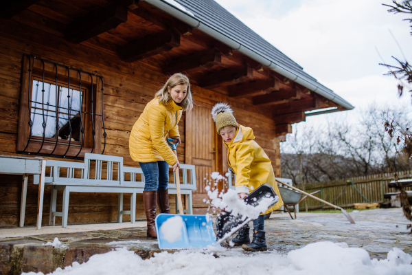 A boy with Down syndrome with his mother clearing snow from path with shovel in front of house.