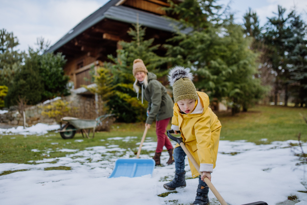 A boy with Down syndrome with his mother clearing snow from path with shovel in front of house.