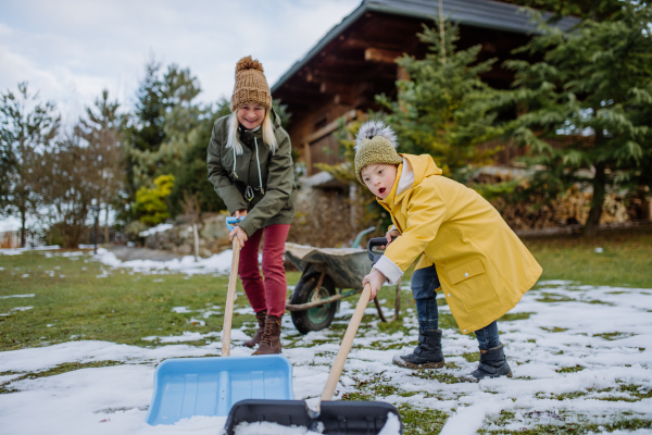 A boy with Down syndrome with his mother clearing snow from path with shovel in front of house.