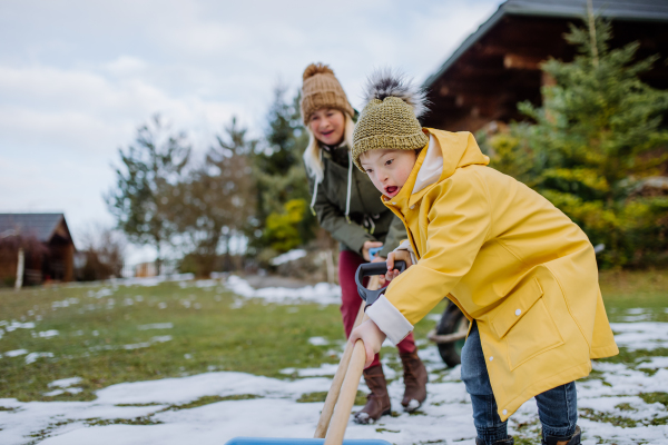 A boy with Down syndrome with his mother clearing snow from path with shovel in front of house.