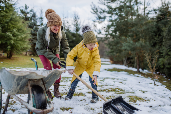 A boy with Down syndrome with his mother clearing snow from path with shovel in front of house.