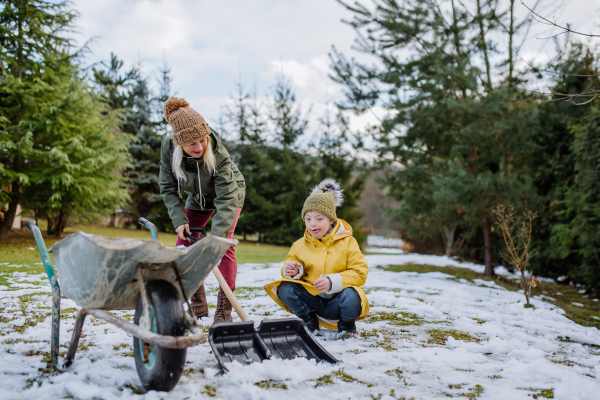 A boy with Down syndrome with his grandmother clearing snow in garden.