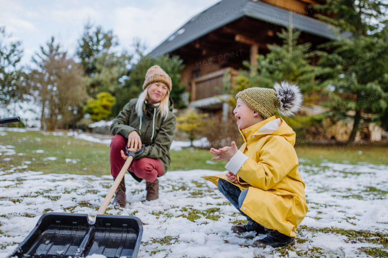 A boy with Down syndrome with his mother clearing snow from path with shovel in front of house.