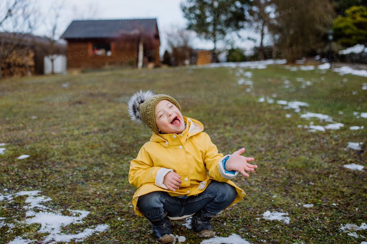 A happy little boy with Down syndrome outside in garden in wnter having fun.