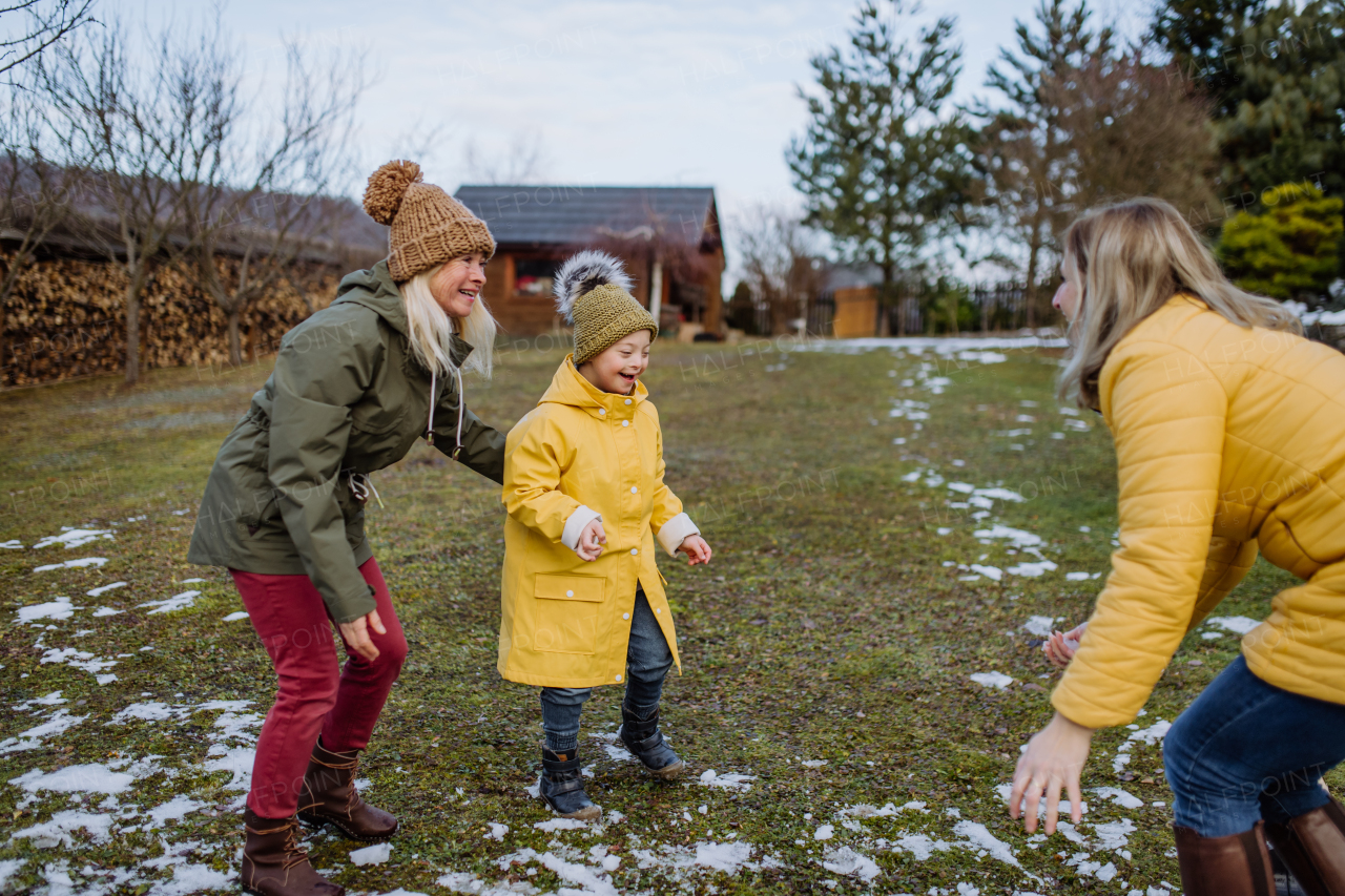 A boy with Down syndrome with his mother and grandmother playing in garden in winter.