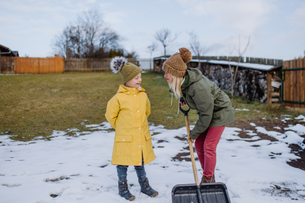 A boy with Down syndrome with his mother clearing snow from path with shovel in front of house.