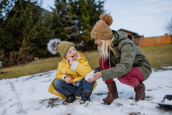 A boy with Down syndrome with his mother playing with snow in garden.