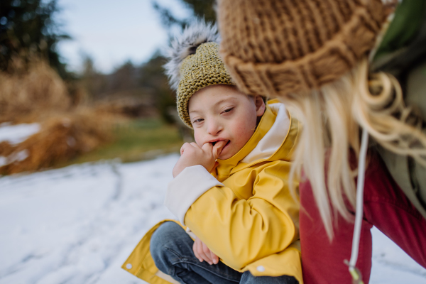 A boy with Down syndrome with his mother playing with snow in garden.