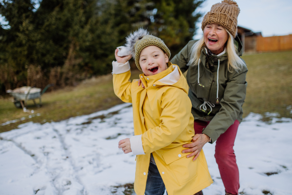 A boy with Down syndrome with his mother playing with snow in garden.