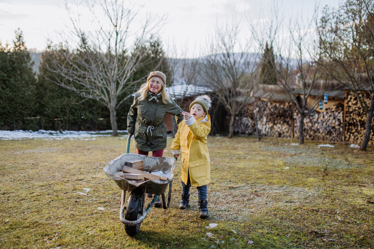 A boy with Down syndrome working in garden in winter with his grandmother.