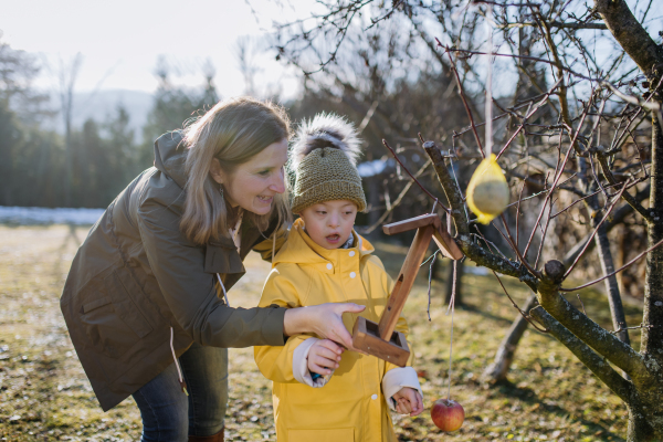 A boy with Down syndrome feeding birds in garden in winter with his mother.