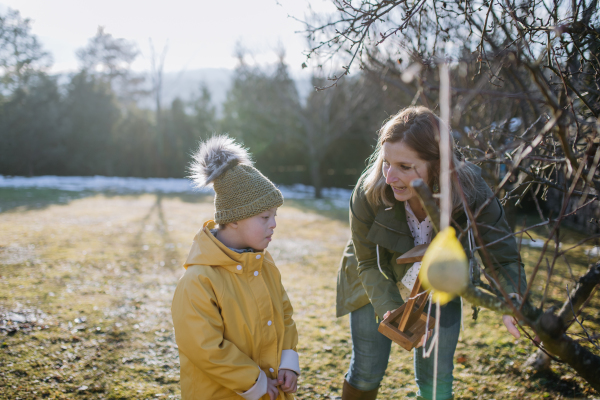 A boy with Down syndrome feeding birds in garden in winter with his mother.