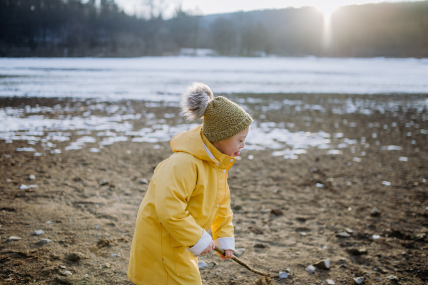 A happy little boy with Down running outside by lake in winter.