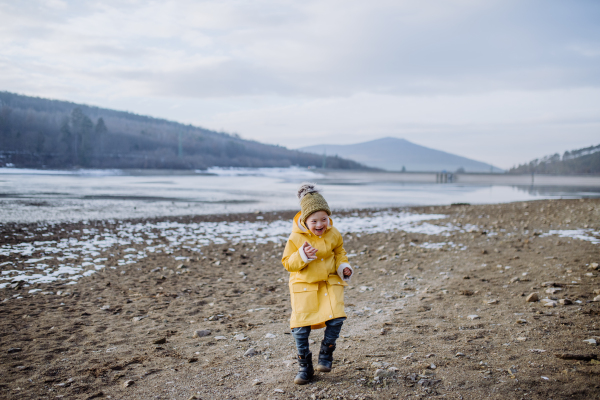 A happy little boy with Down running outside by lake in winter.