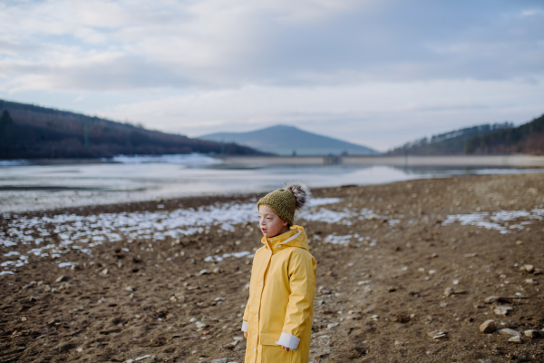 A Sad little boy with Down running outside by lake in winter.