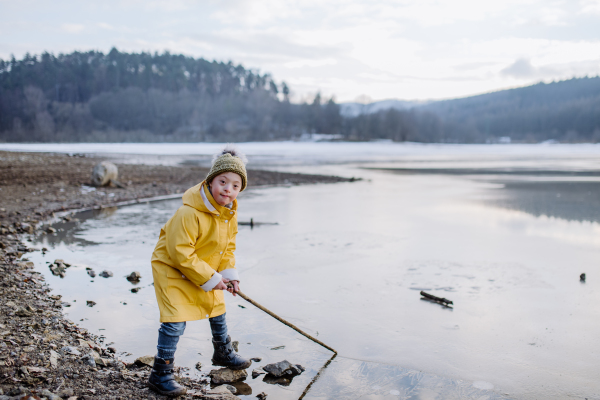 A happy little boy with Down syndrome looking at camera outside by lake in winter.