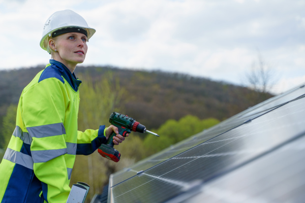 A woman engineer installing solar photovoltaic panels on roof, alternative energy concept.