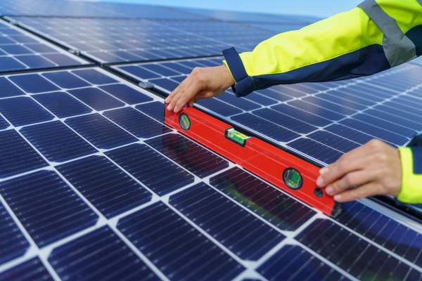 A close-up of woman engineer measuring solar photovoltaic panels on roof, alternative energy concept.