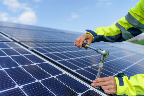 A close-up of woman engineer installing solar photovoltaic panels on roof, alternative energy concept.