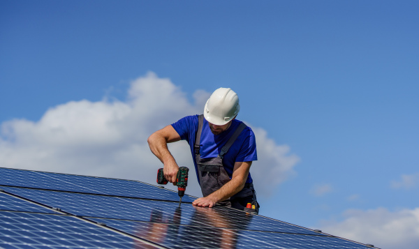 A man worker installing solar photovoltaic panels on roof, alternative energy concept.