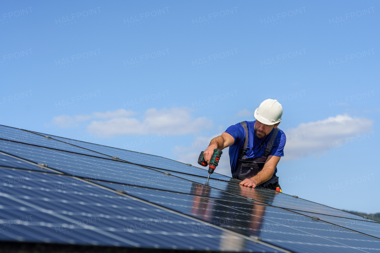 A man worker installing solar photovoltaic panels on roof, alternative energy concept.