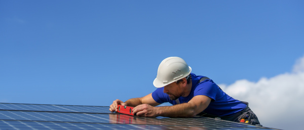 A man worker installing solar photovoltaic panels on roof, alternative energy concept.