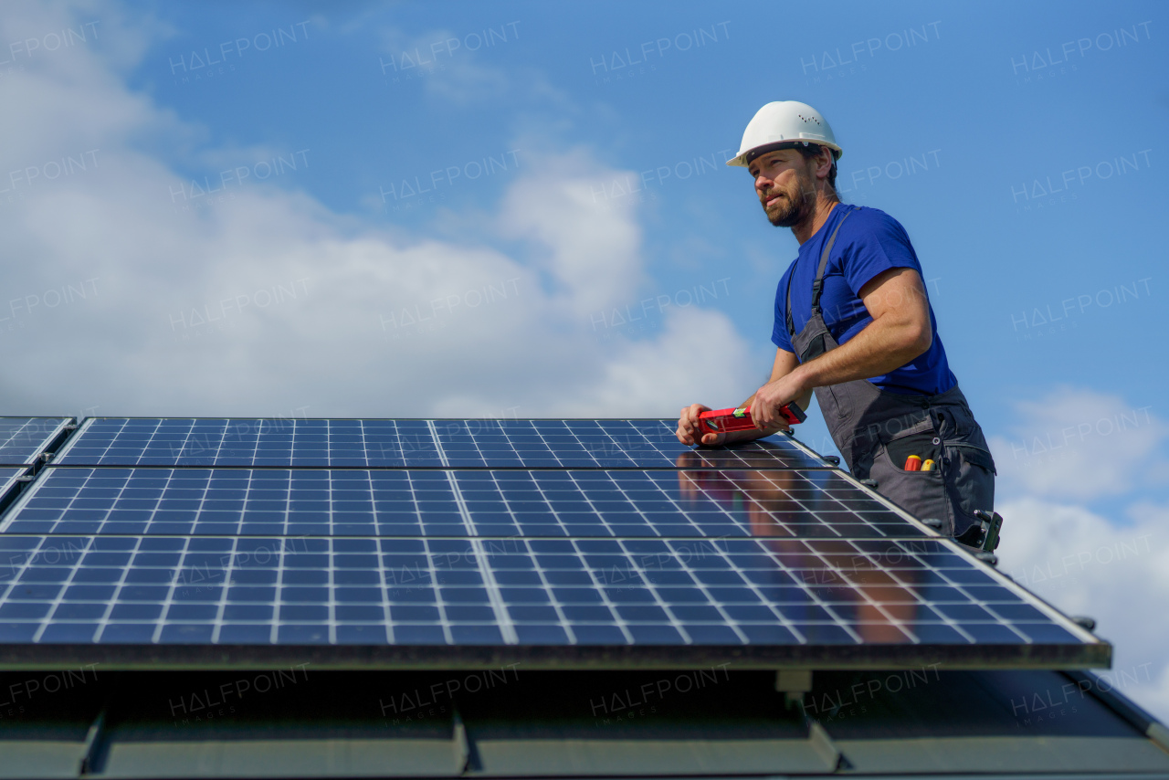 A man worker installing solar photovoltaic panels on roof, alternative energy concept.