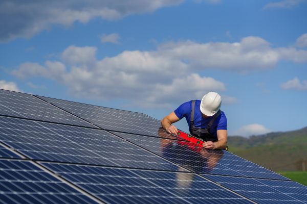 A man worker installing solar photovoltaic panels on roof, alternative energy concept.