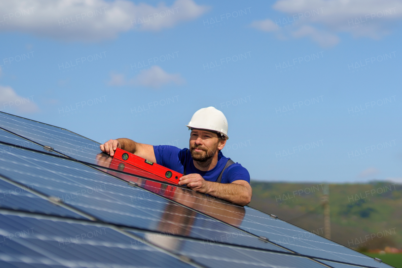 A man worker installing solar photovoltaic panels on roof, alternative energy concept.