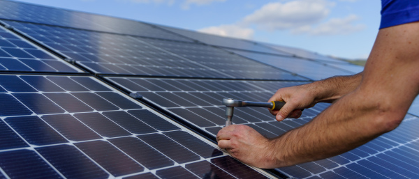 A man worker installing solar photovoltaic panels on roof, alternative energy concept. Close up hands with drill.