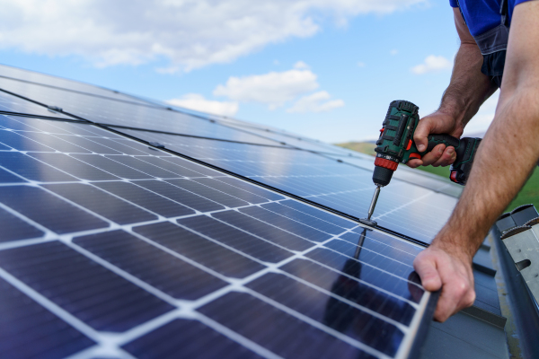 A man worker installing solar photovoltaic panels on roof, alternative energy concept.