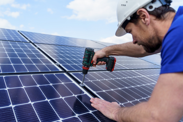 A man worker installing solar photovoltaic panels on roof, alternative energy concept.