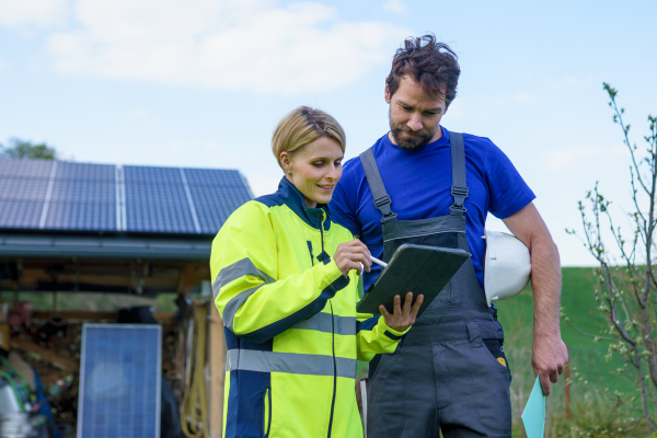 A man and woman solar installers engineers with tablet while installing solar panel system on house.