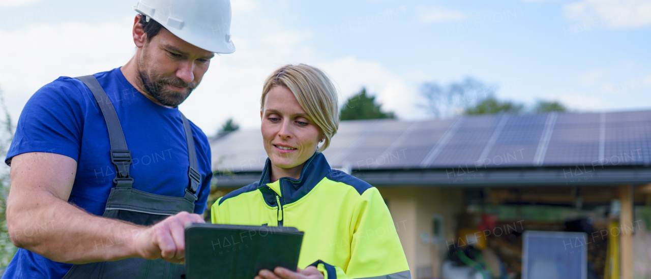 A man and woman solar installers engineers with tablet while installing solar panel system on house.