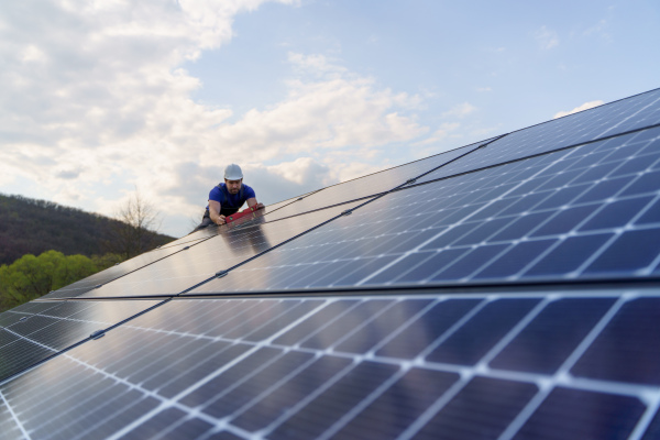 A man worker installing solar photovoltaic panels on roof, alternative energy concept.