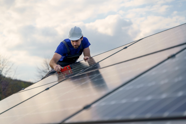 A man worker installing solar photovoltaic panels on roof, alternative energy concept.