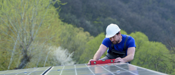 A man worker installing solar photovoltaic panels on roof, alternative energy concept.