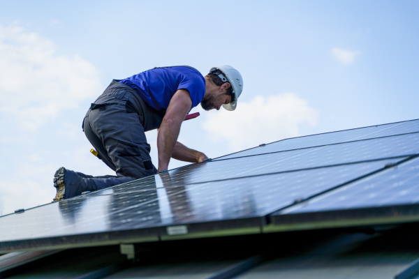 A man worker installing solar photovoltaic panels on roof, alternative energy concept.