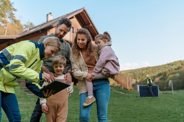 A woman engineer talking to young family about solar panel installation in front of their house.