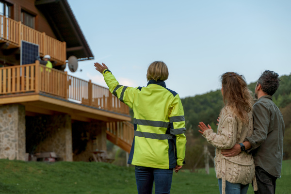 A woman engineer talking to couple about solar panel installation in front of their house.