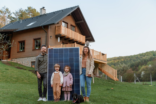 A happy family near their house with solar panels. Alternative energy source