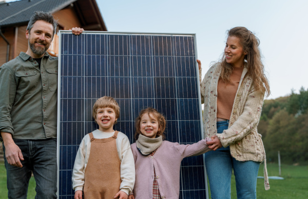 A happy family near their house with solar panels. Alternative energy source