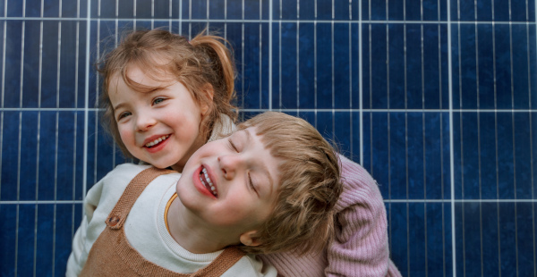 A portrait of happy little siblings in front of solar panel, alternative energy source concept.