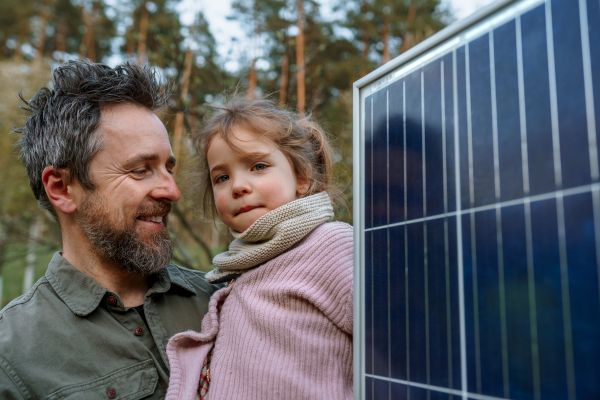 A portrait of father and daughter holding a solar panel in garden.