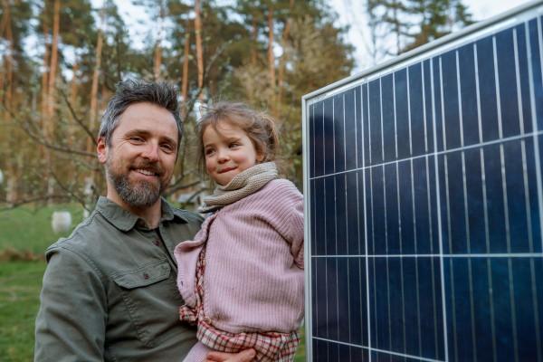 A portrait of father and daughter holding a solar panel in garden.