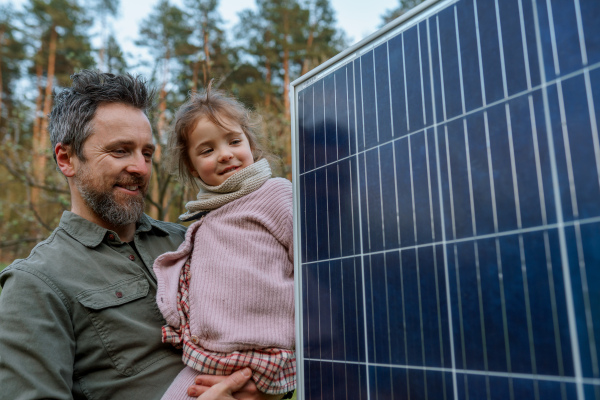 A portrait of father and daughter holding a solar panel in garden.