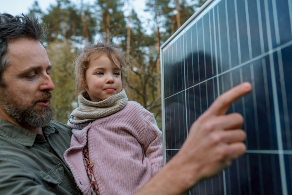 A portrait of father and daughter holding a solar panel in garden.