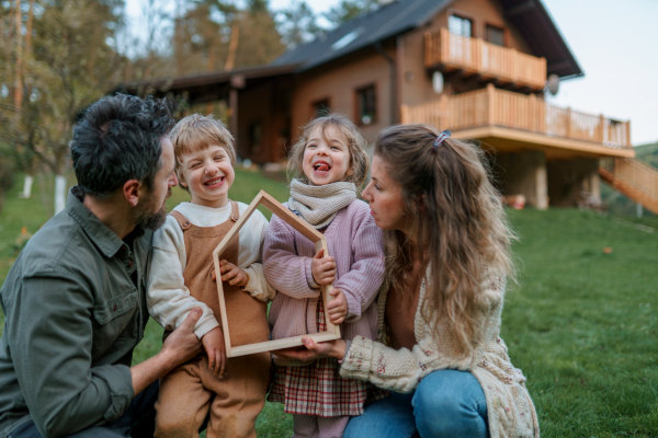 A happy family is standing near their modern house, smiling and looking at camera