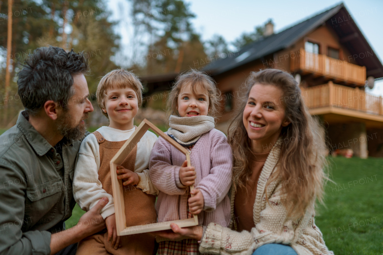 A happy family is standing near their modern house, smiling and looking at camera